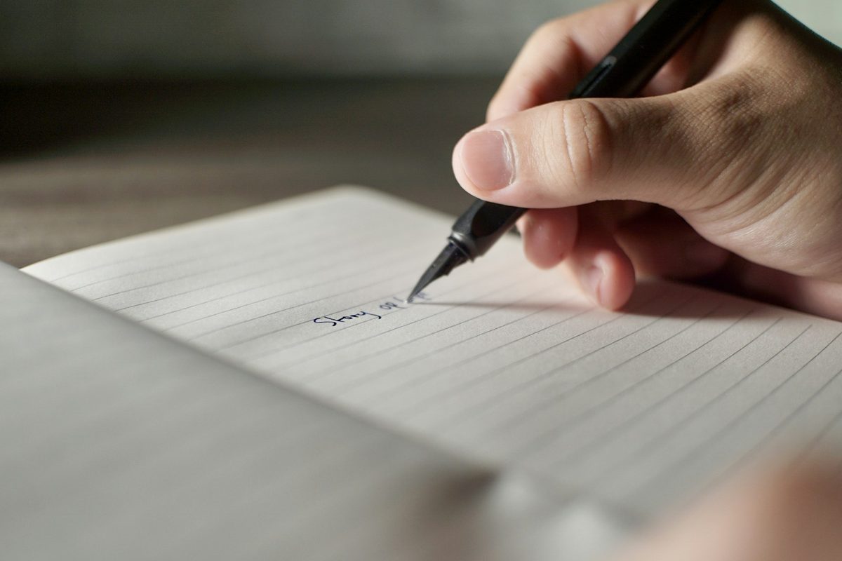 A hand marking a symbol on ruled paper with a fine pen