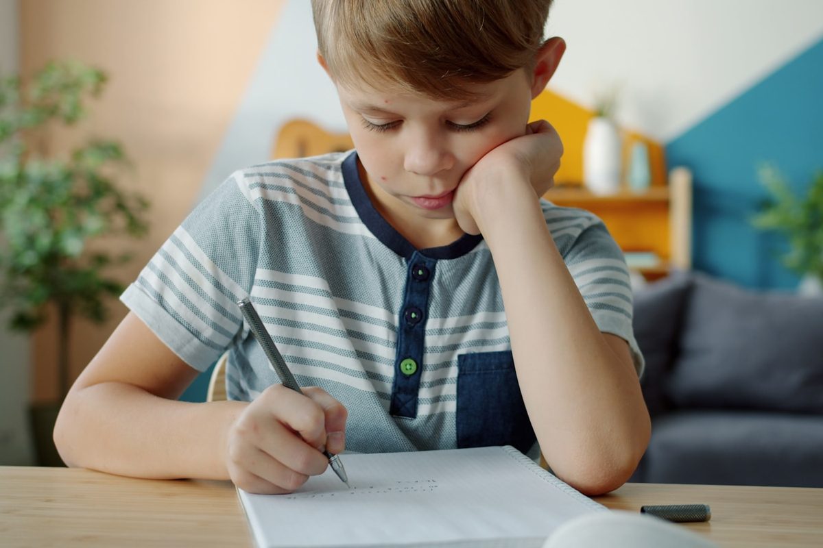A boy resting his head on one hand while writing at a desk