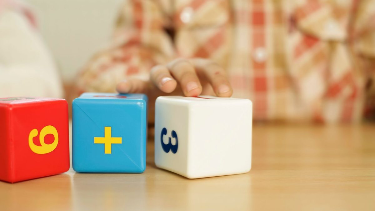 A child's hand touching educational math blocks on a desk