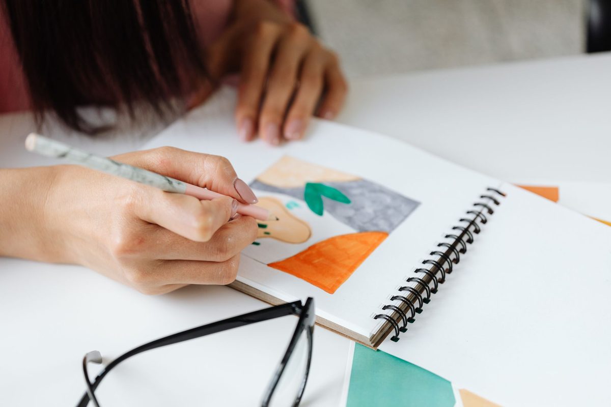 A child's hands drawing and cutting shapes at a notebook on a table