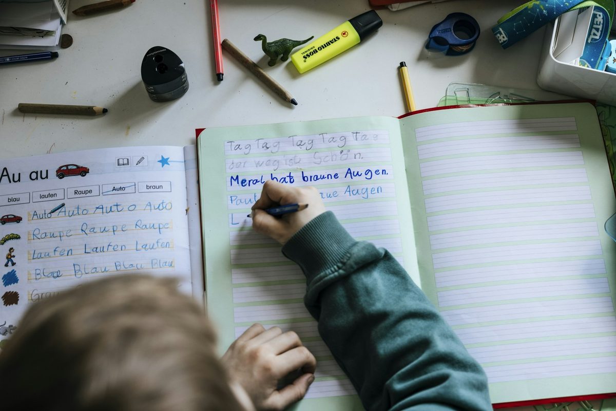 A young child writing letters into a ruled exercise book at a desk