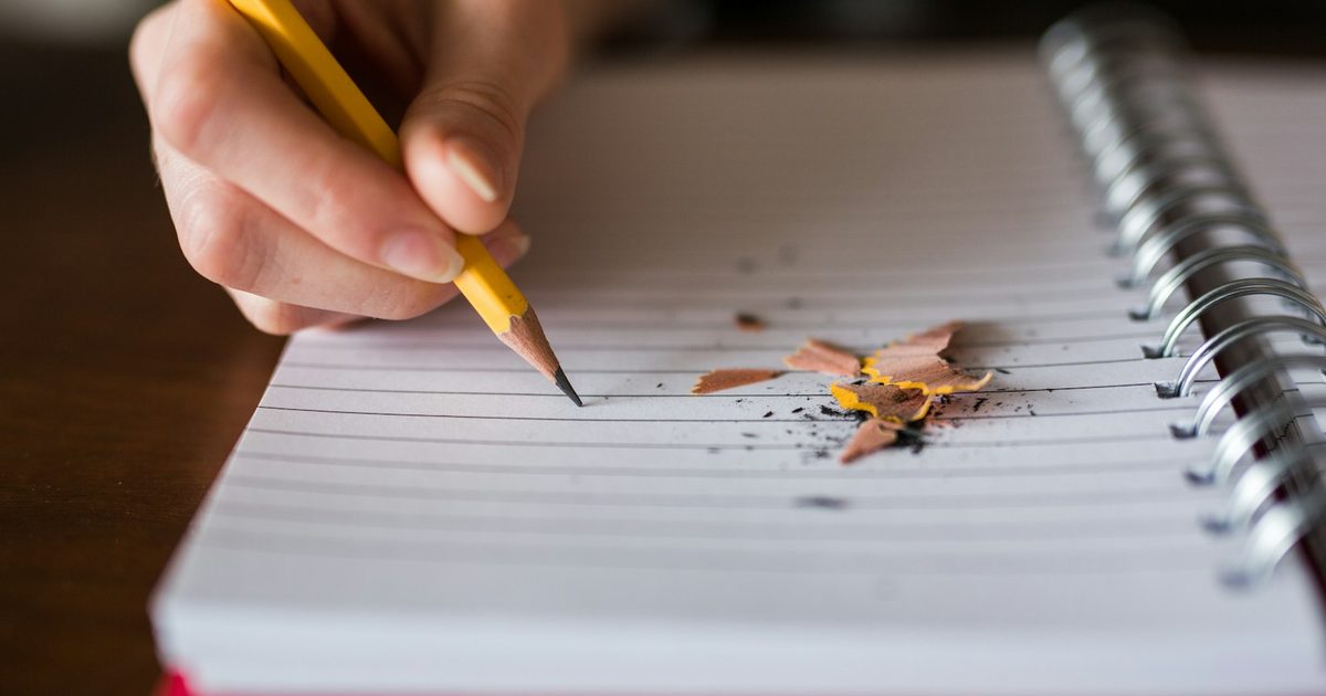 A single pencil held in a hand above an empty desk