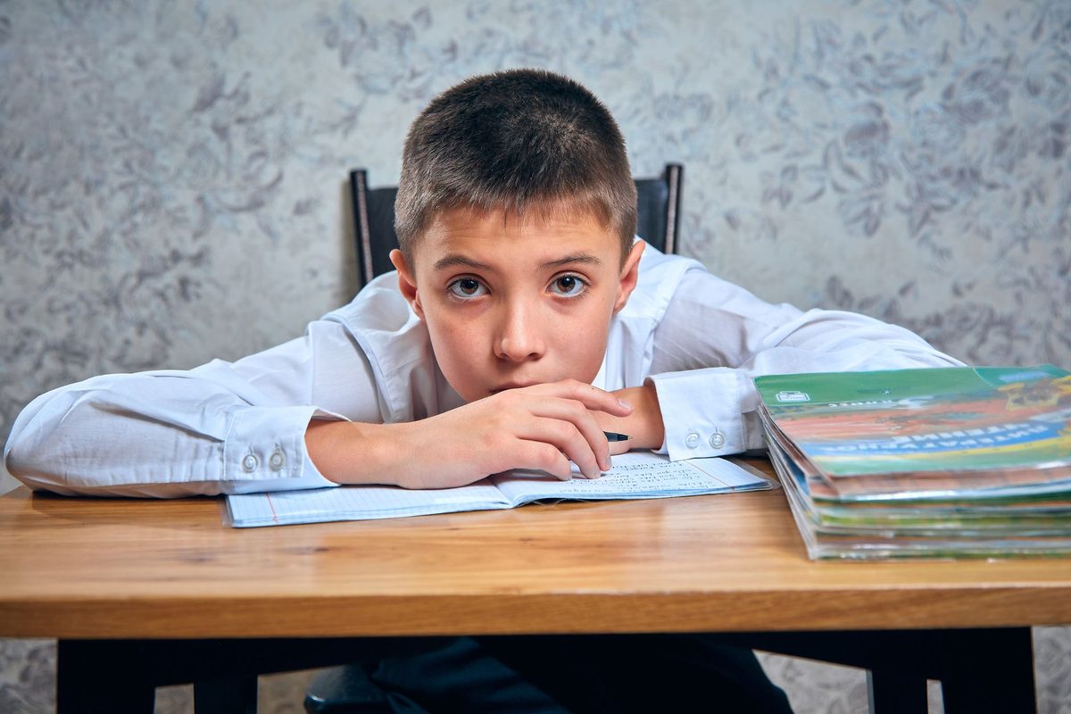 A boy sitting at a desk with his hands clasped in front of a workbook