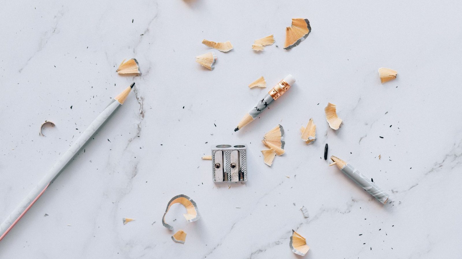 Sharpened pencils and shavings arranged neatly on a pale marble surface