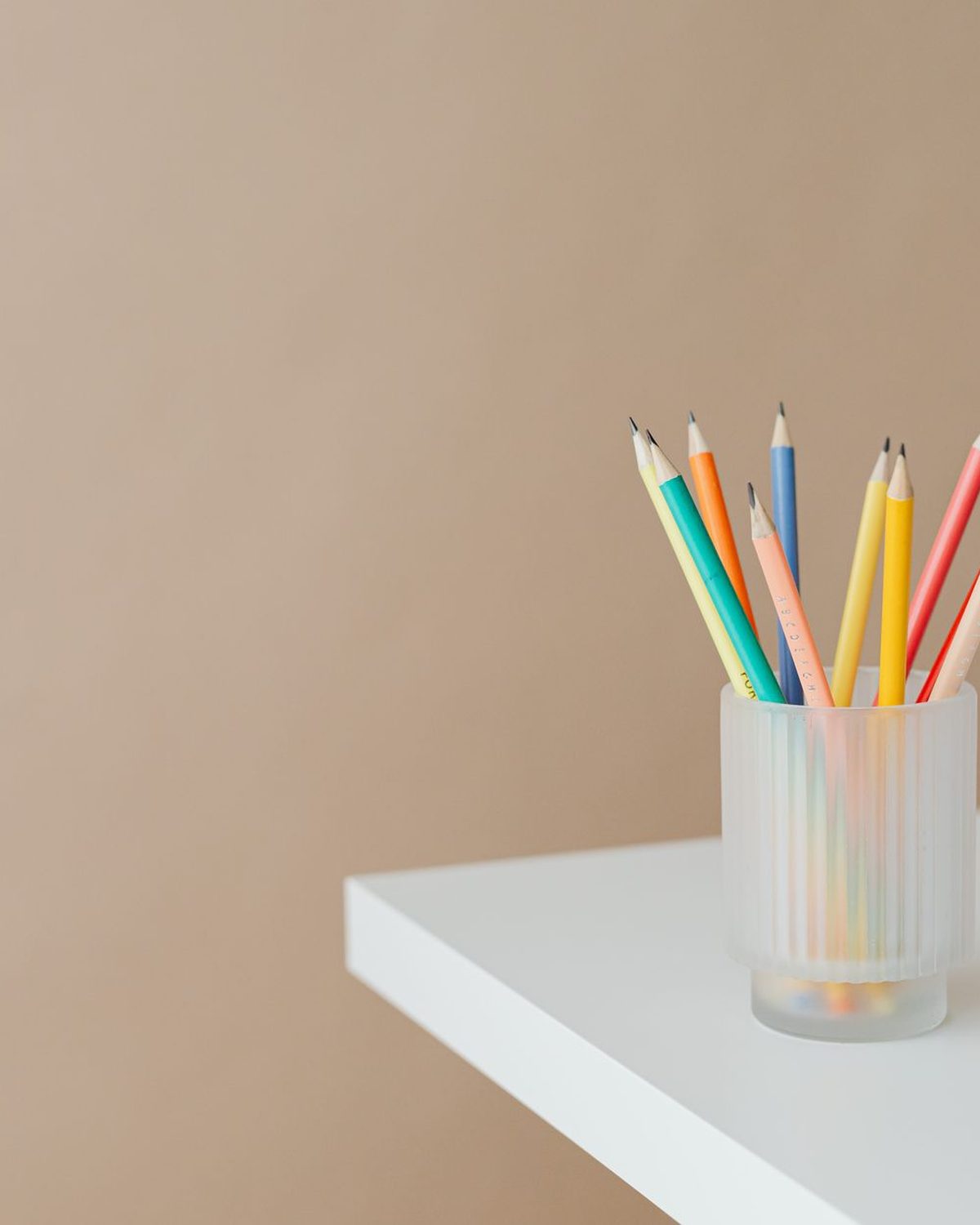 Coloured pencils standing together in a holder on a minimal surface