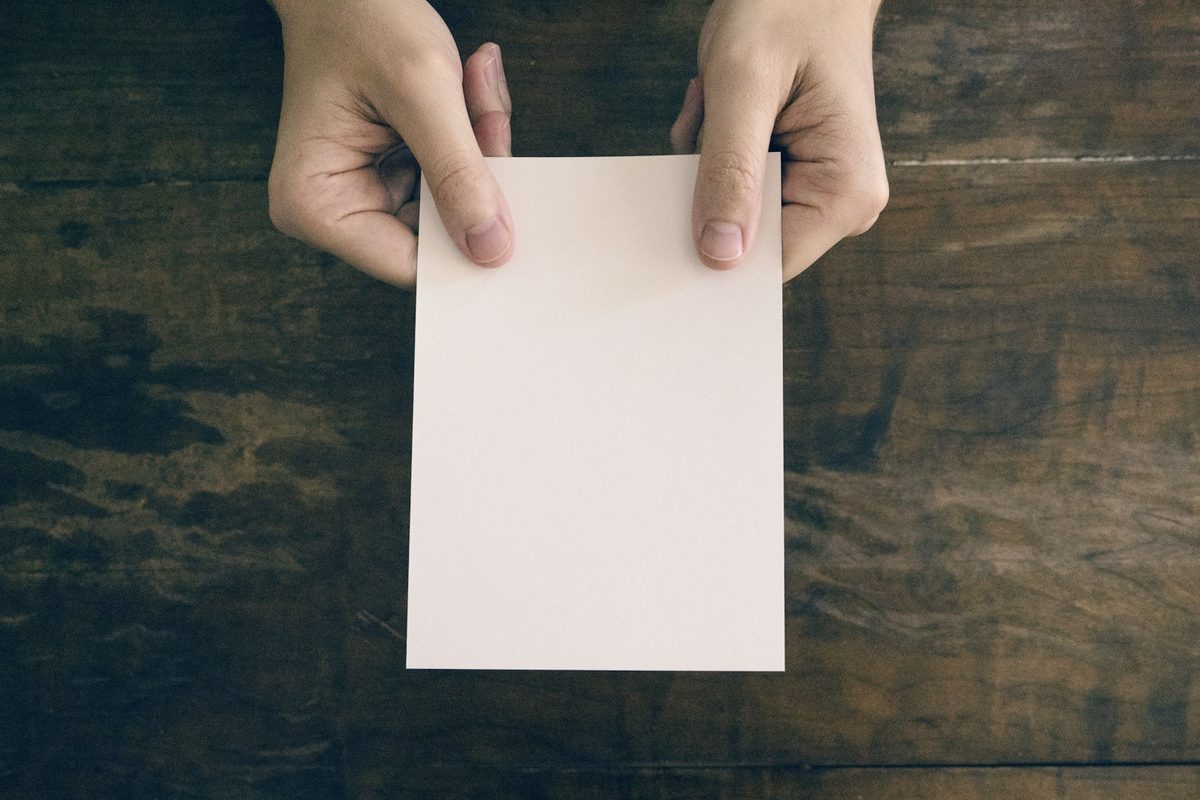 Two hands pressing a fold into a sheet of pale paper on a wooden surface