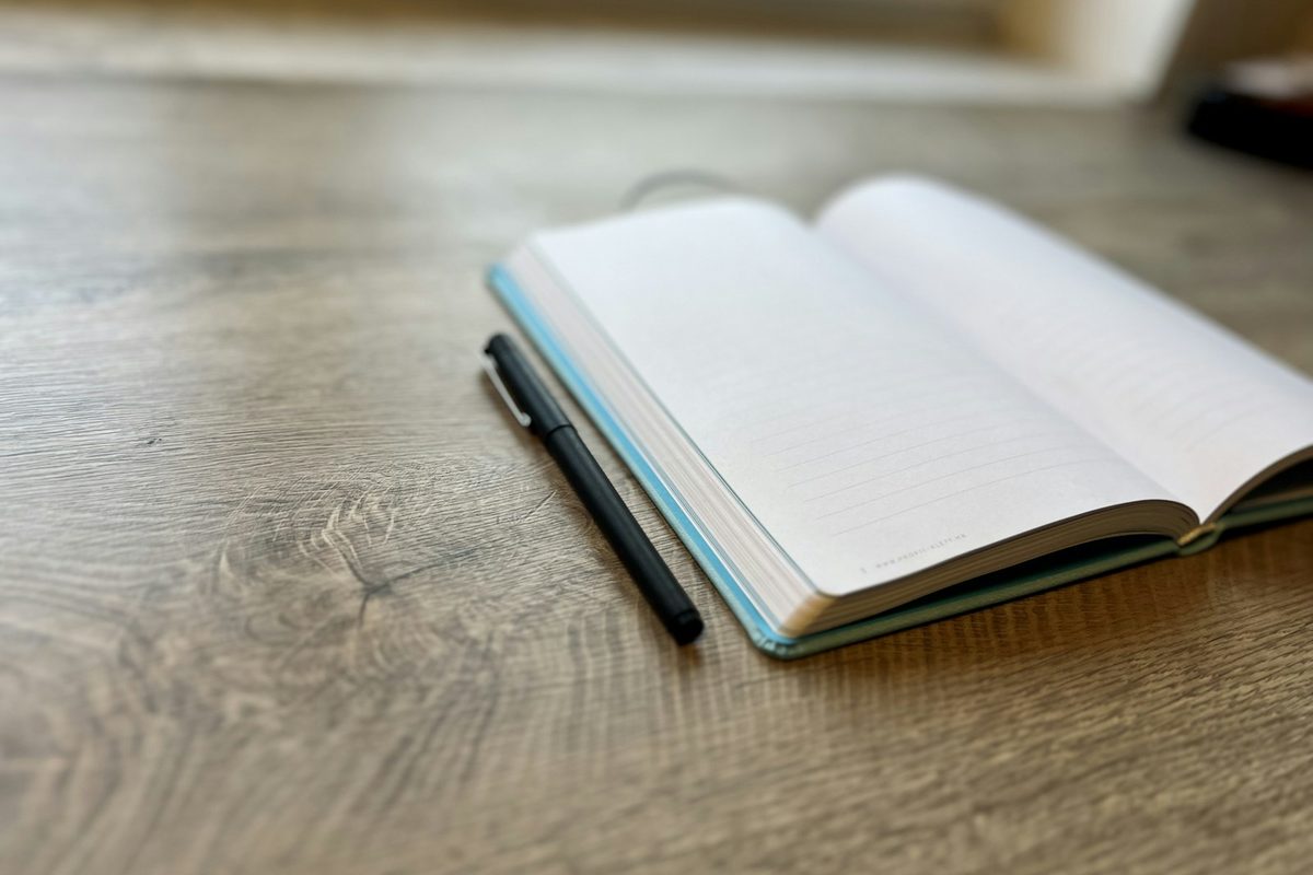 An open notebook with a pen resting on it on a wooden desk