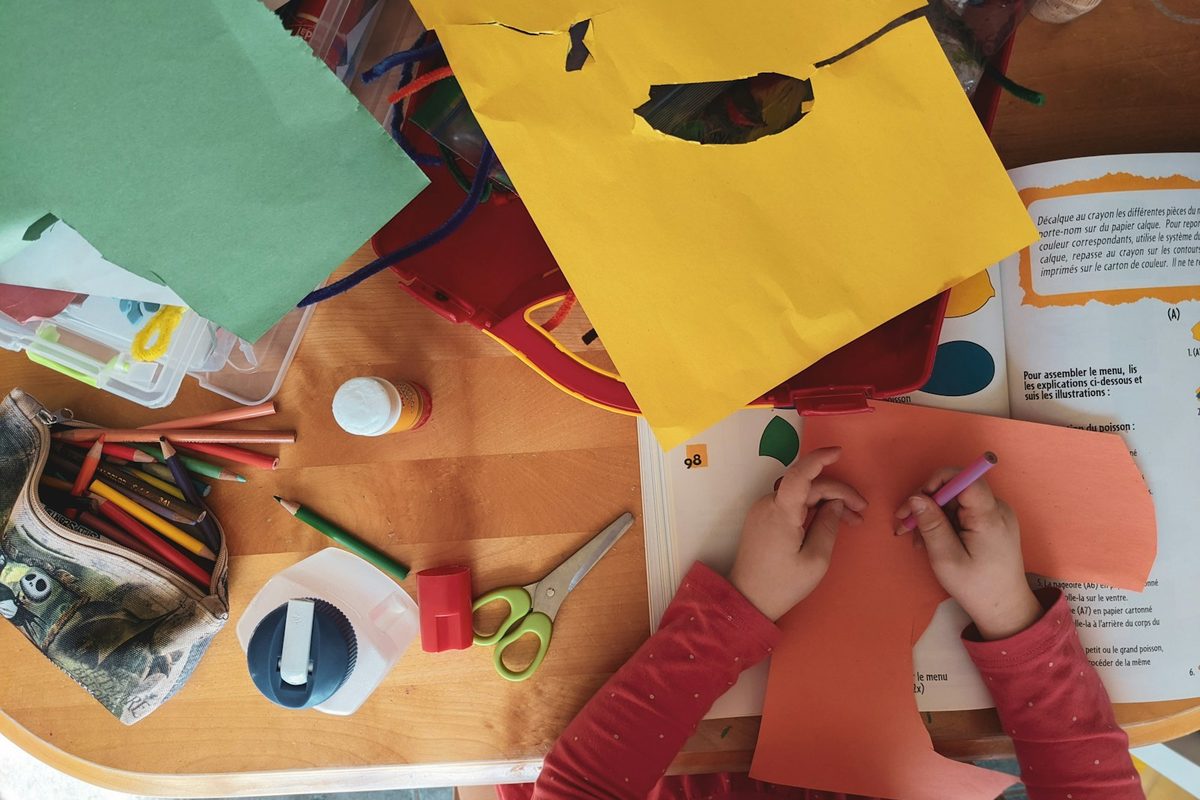 A child's hands folding a sheet of coloured paper into a shape