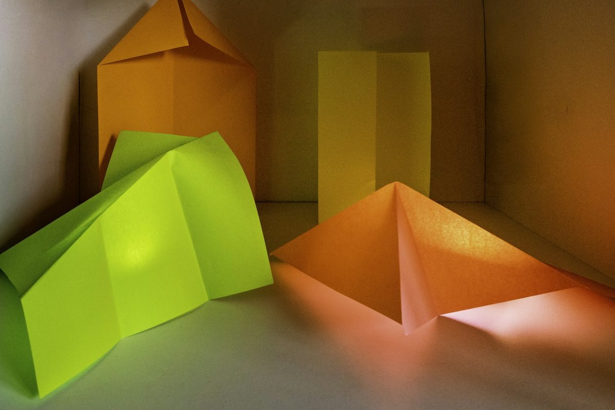 Folded paper forms in green and orange arranged together under warm light