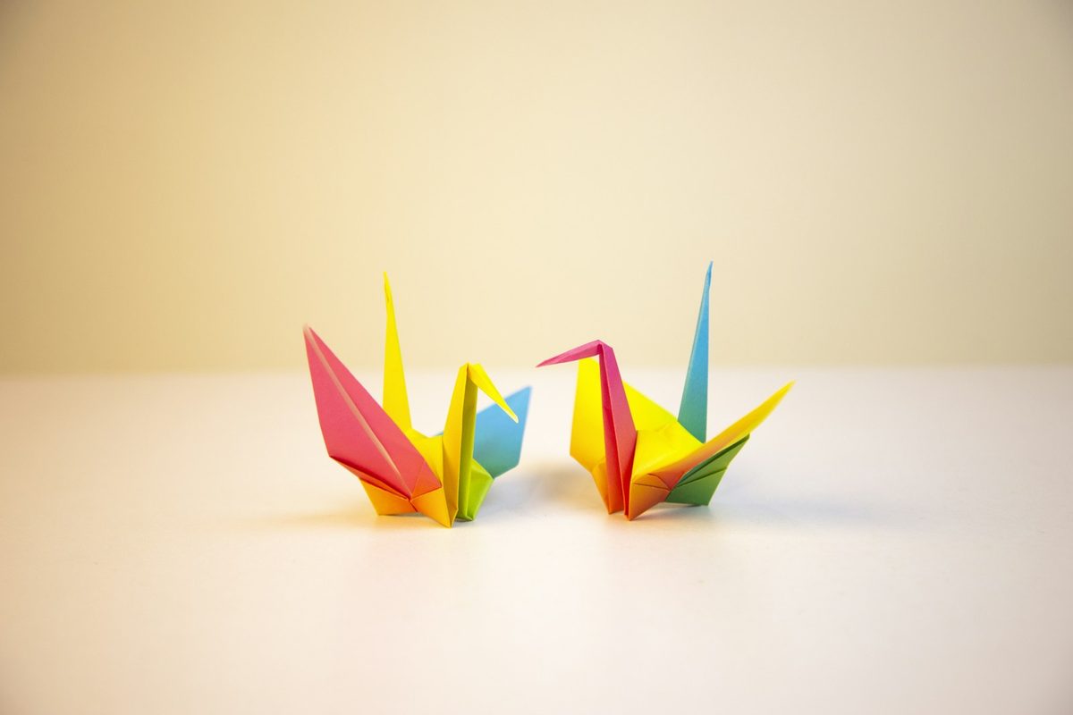 Three brightly coloured origami paper cranes standing on a pale surface