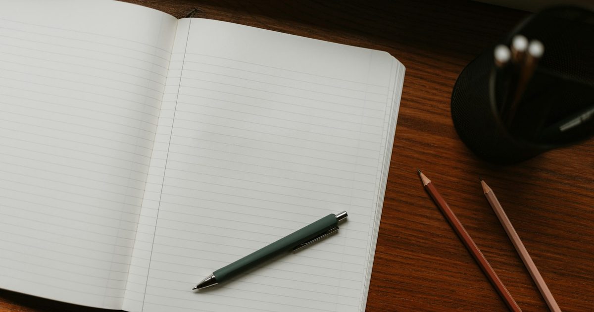 An open notebook and pen on a wooden desk ready for a paper game