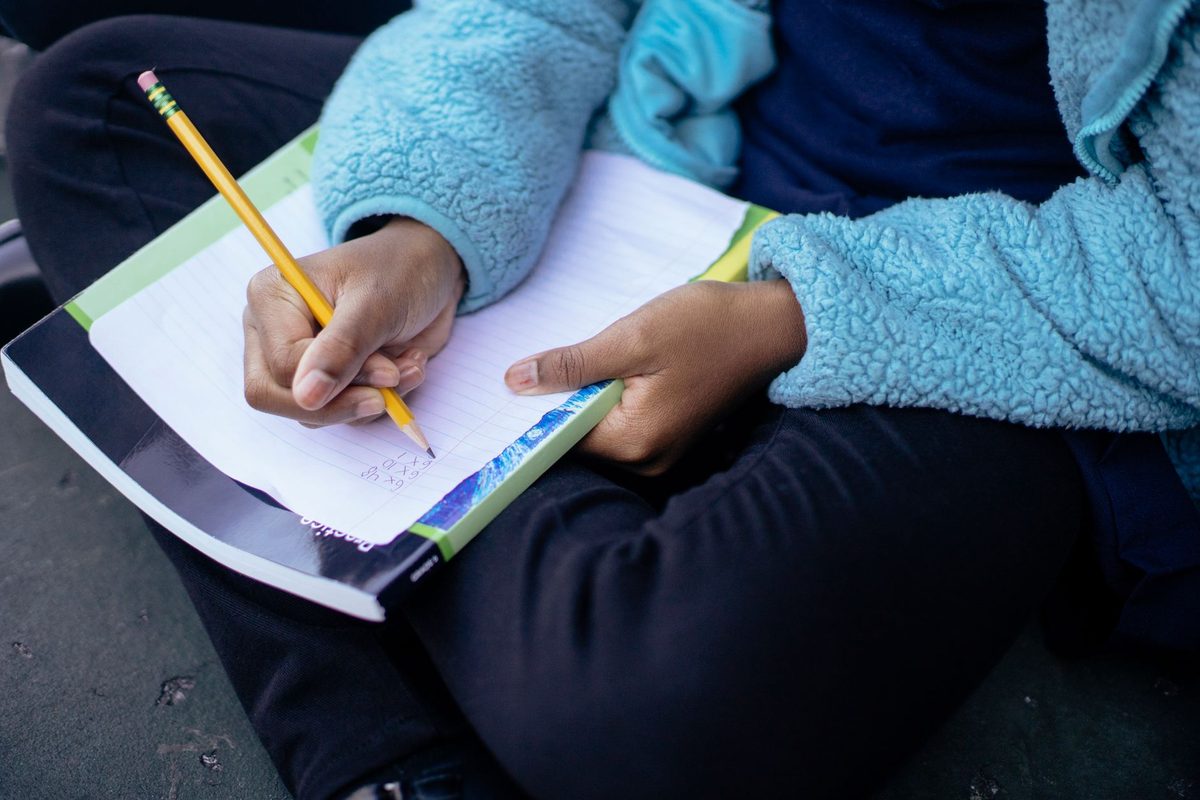 A child writing in an exercise book while holding a yellow pencil