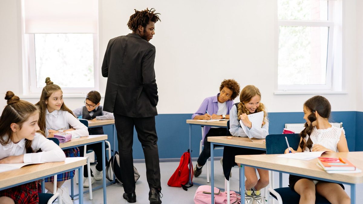 A teacher supervising pupils working at their desks in a bright classroom