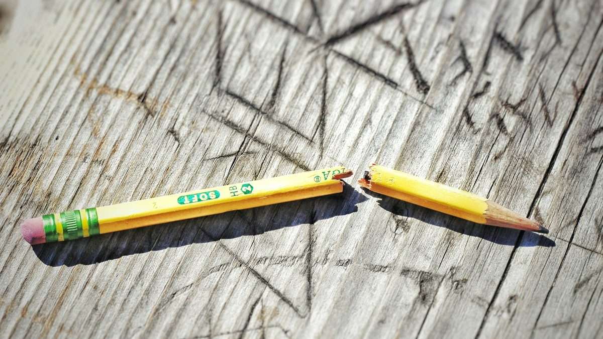 A yellow HB pencil snapped cleanly in two on a weathered wooden surface, showing the splintered break