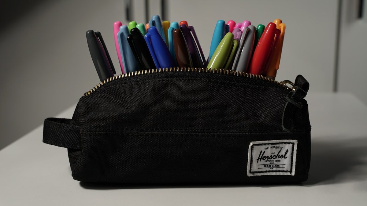 A black desk pot filled with pens, pencils and markers