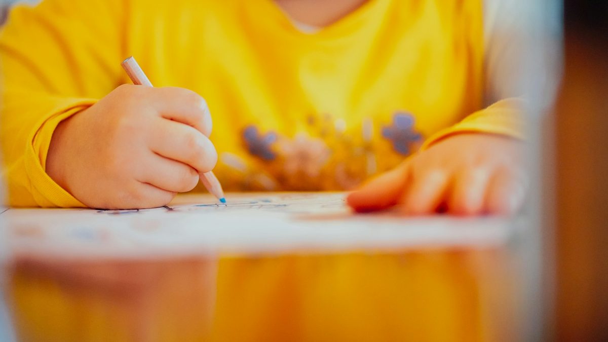 A child writing in an exercise book with a pencil