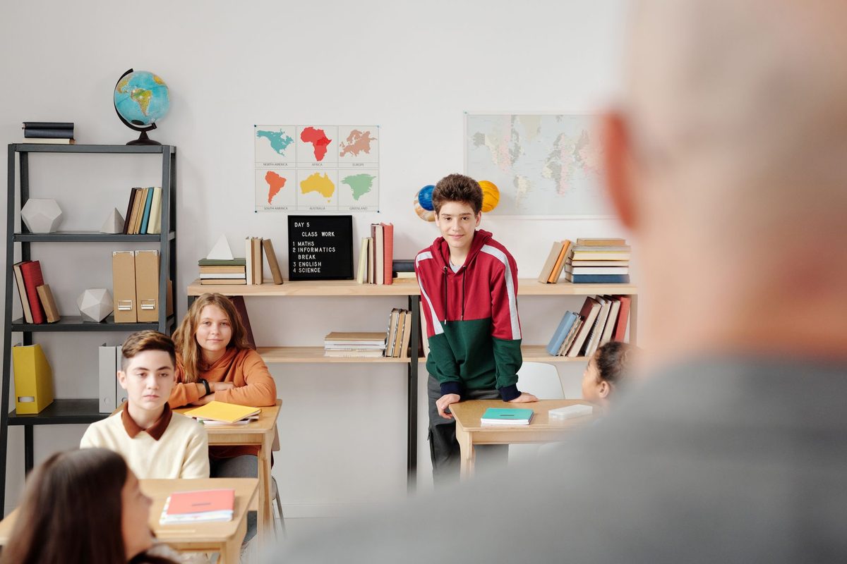 A teacher standing at the front of a classroom watching pupils at work