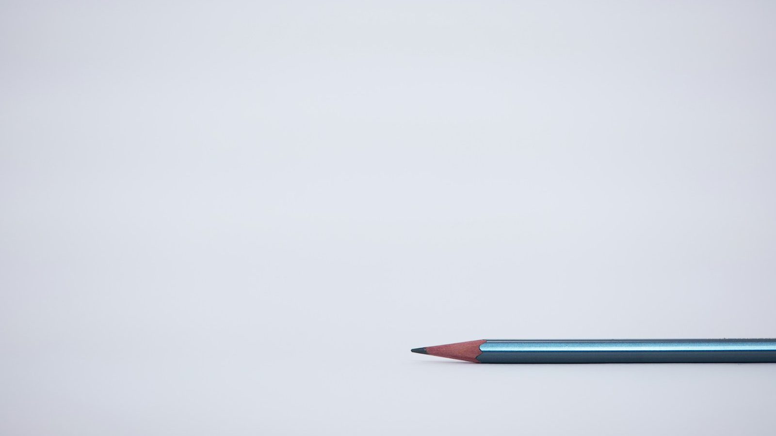 A single sharpened pencil resting on a clean pale surface
