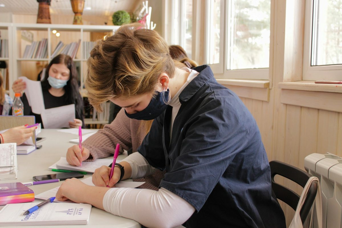 Two children sitting at a table writing and drawing on paper together