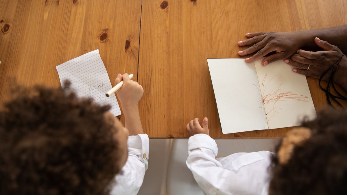 Two children sitting at a table writing and playing together